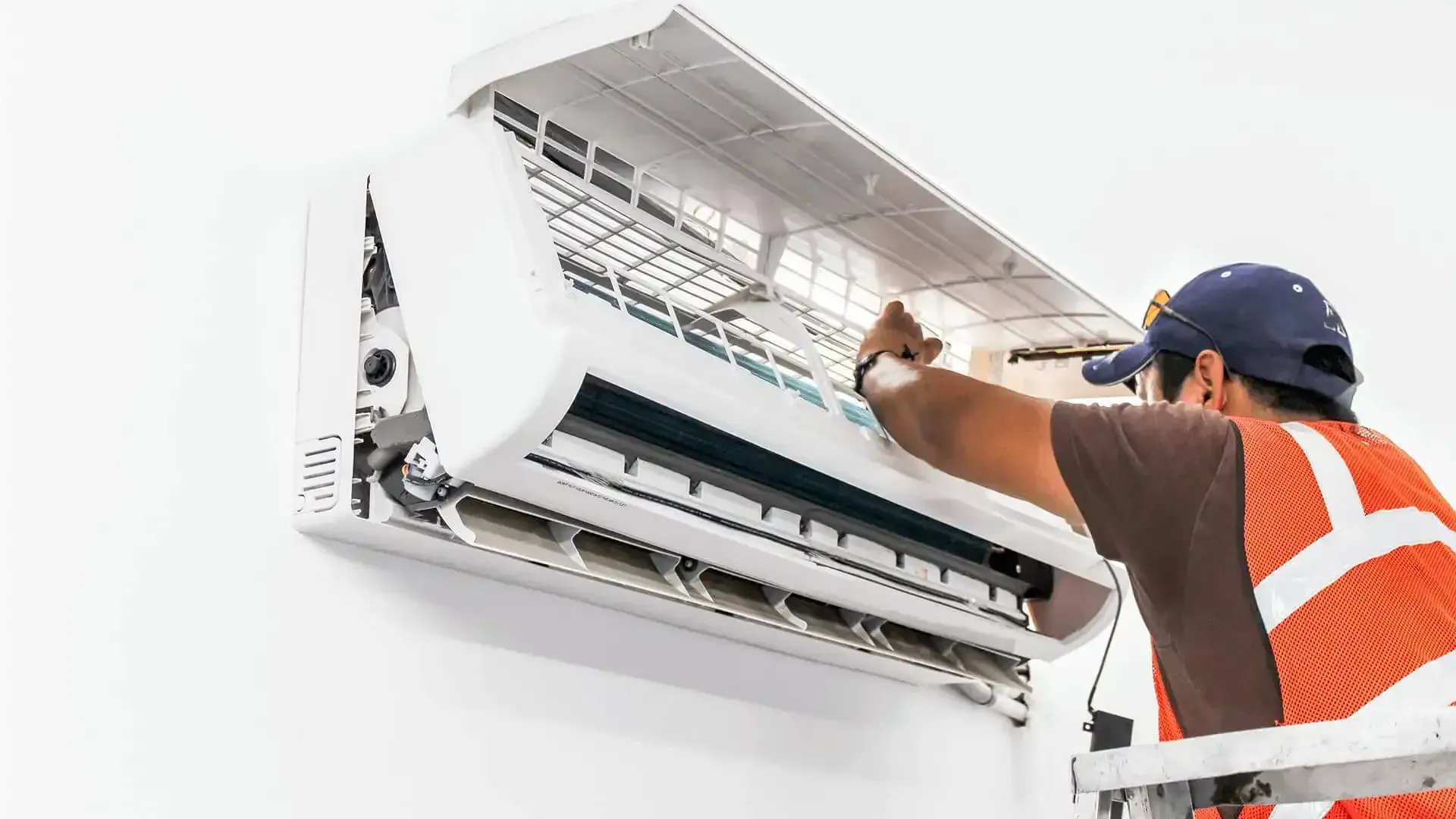 Technician repairs a white air conditioner unit mounted on a wall.
